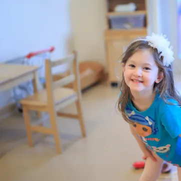 A young girl in a blue tshirt and white flower headband smiles for the camera at a YMCA Child Care Centre.