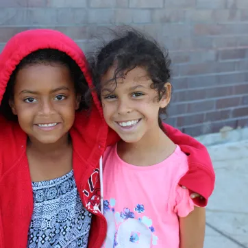 A girl in a red hoodie puts her arm around her friend in a pink t-shirt at YMCA Day Camp.