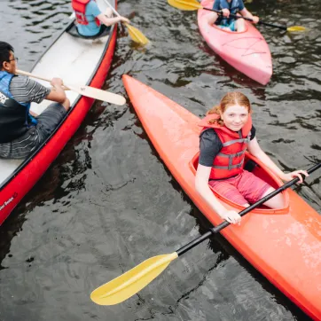 A group of kids paddle on the lake in canoes and kayaks.