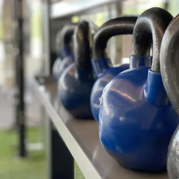 A row of blue and grey kettlebells sits in the turf fitness zone area of a YMCA.