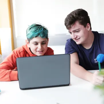 Two teenage boys watch something on a laptop.