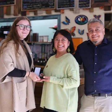 Group of three people standing together, one woman is presenting a medal to another. 